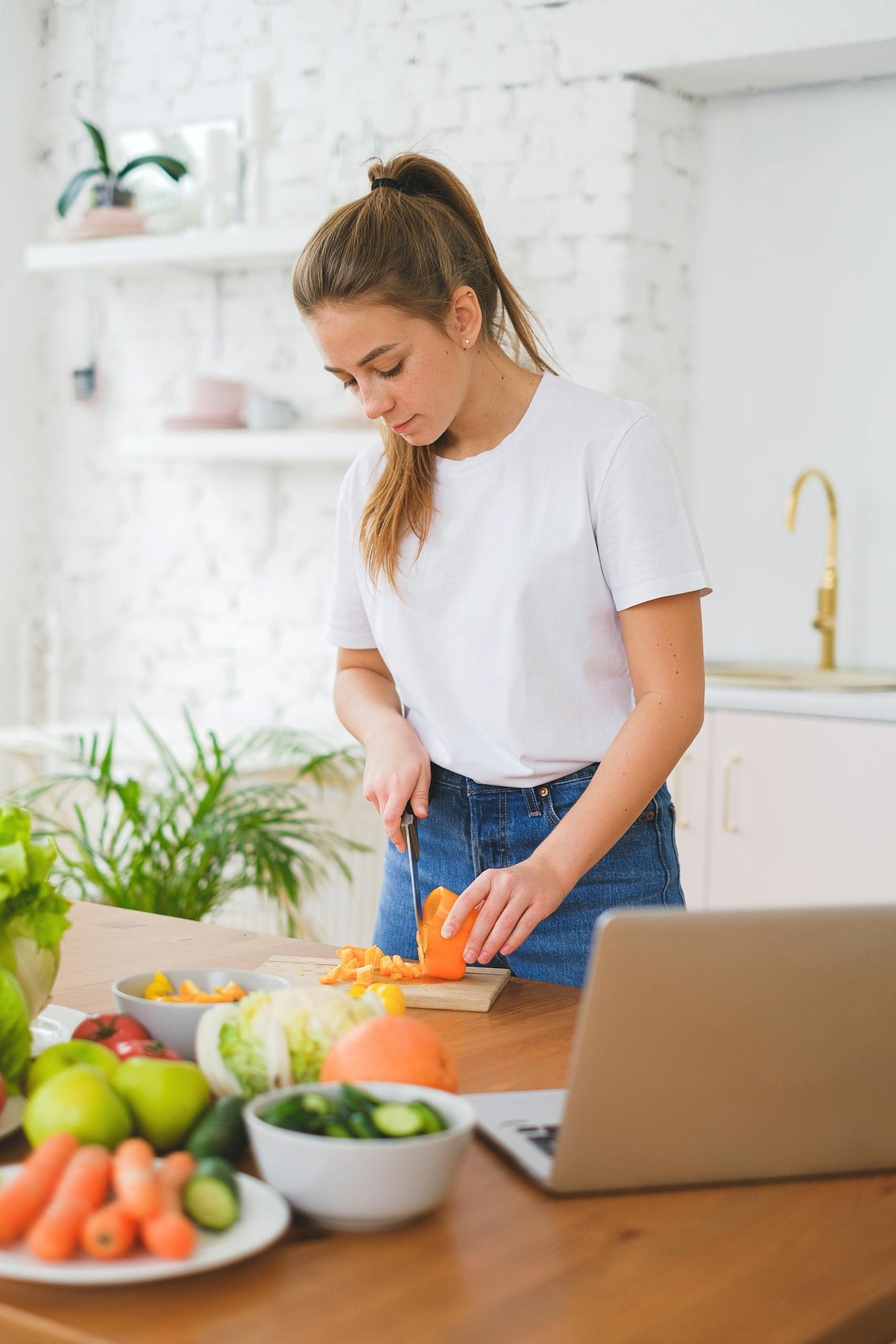 Caucasian woman slicing vegetables in a bright, modern kitchen for a fresh salad.